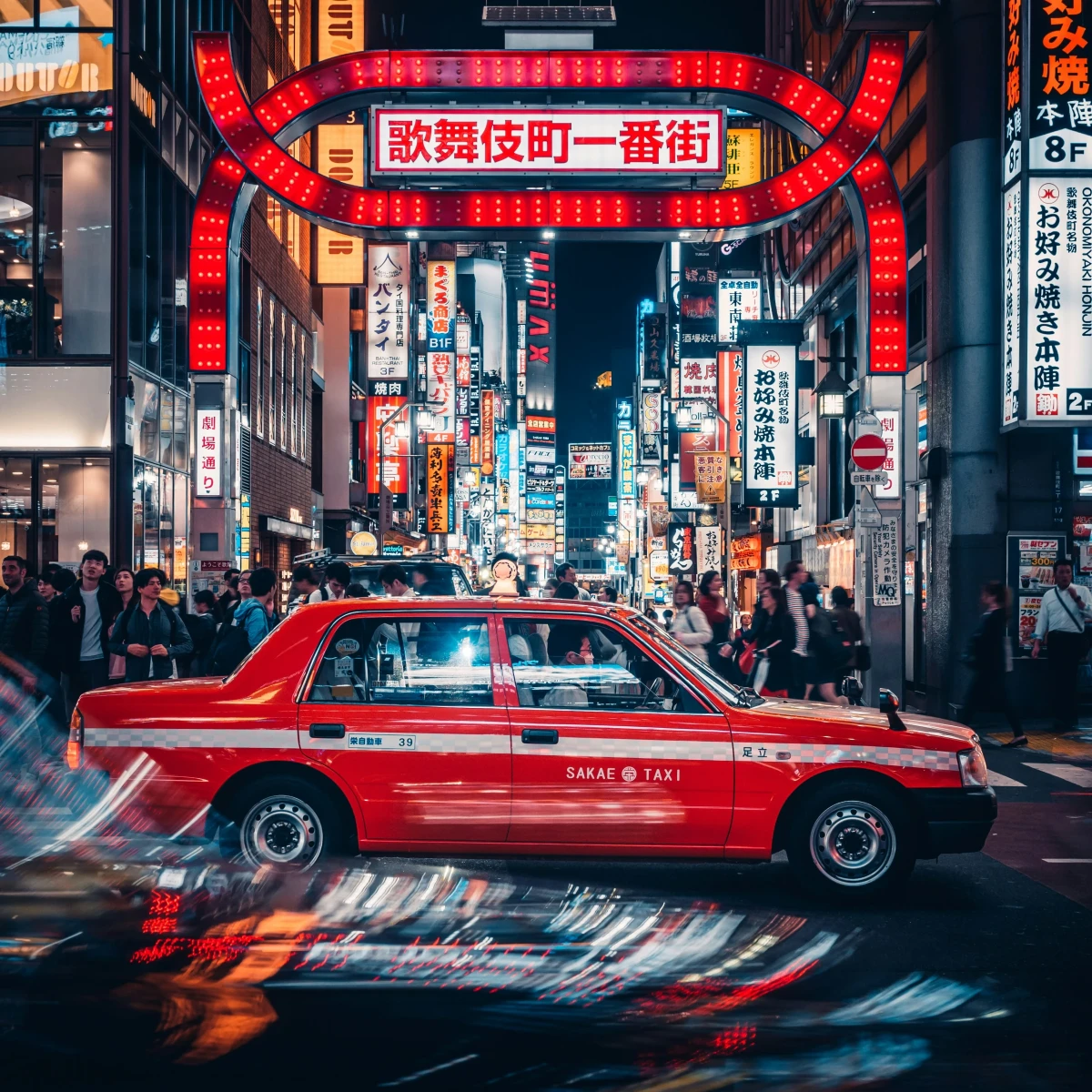 Rotes Taxi auf einer belebten Stra&szlig;e in Tokio, Japan, mit leuchtenden Neonlichtern und japanischen Schriftzeichen im Hintergrund des n&auml;chtlichen Stadtviertels.